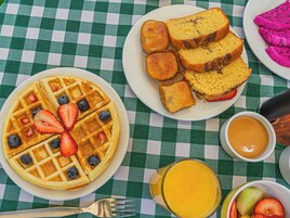Una mesa de desayuno con waffles, muffins, tostadas y fruta.