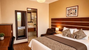 A hotel room with a bed, a desk, a chair, a mirror, and a painting on the wall. - Casa de Avila Hotel (Arequipa)