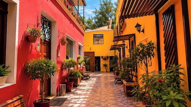 A narrow alleyway with buildings painted in red and yellow, potted plants, and a bench. - Casa de Avila Hotel (Arequipa)