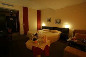 Habitación de hotel con cama, mesita de noche y una mesa con una botella, vasos y un plato.
