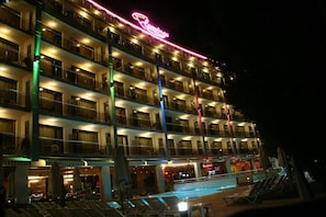 A multi-story hotel with balconies, a pool area, and a neon sign.