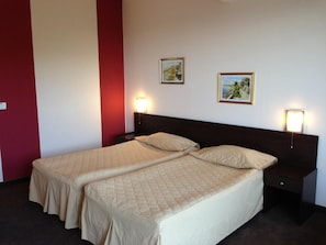 A hotel room with two beds, a red accent wall, and two framed pictures on the wall.