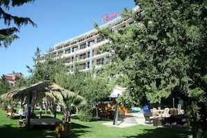 Un hotel de varios pisos, con mobiliario exterior y una estructura de techo de paja.