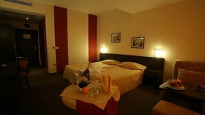 A hotel room with a bed, bedside tables, a small table with a bottle, glasses, and a plate of food. - Flamingo (Nessebar)