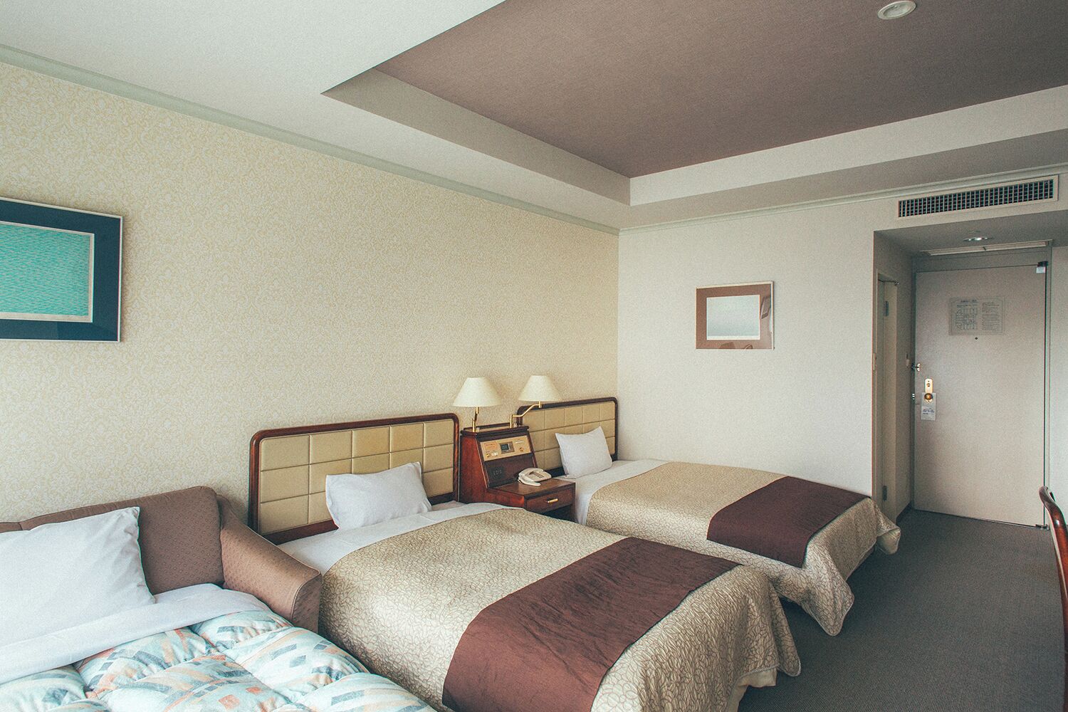 A hotel room with two beds, a nightstand with lamps, a framed picture on the wall, and a door with a lock.