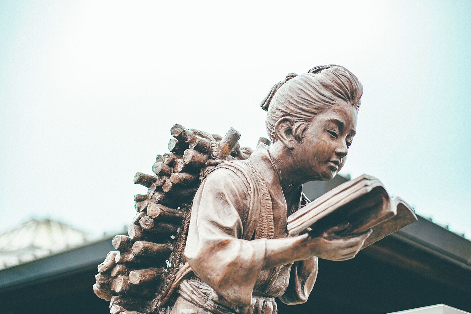 A statue of a person with a large backpack made of logs, holding a book.