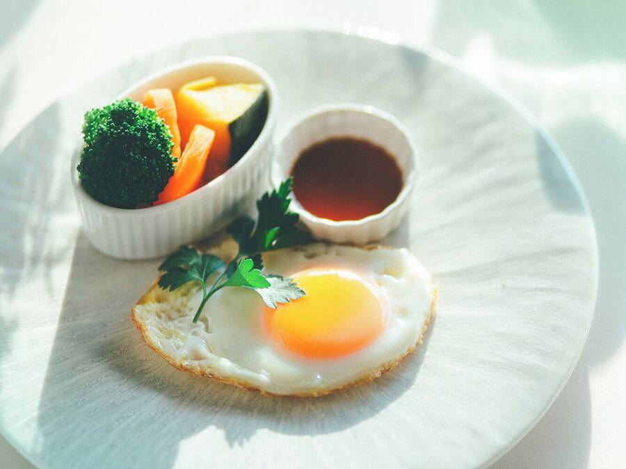 A plate with a sunny side-up egg, a bowl of mixed vegetables, and a small cup of sauce.