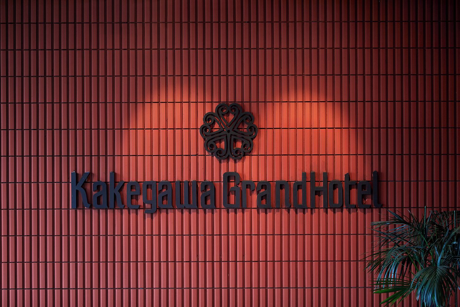 Uma parede vermelha com o texto "Kakegawa Grand Hotel" e um emblema decorativo.