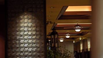 A corridor with a brick wall on the left and hanging lights on the ceiling.