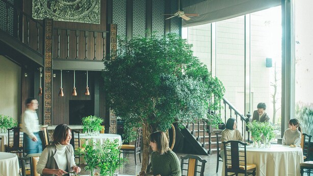 Restaurante com mesas redondas, plantas dentro e uma escadaria.
