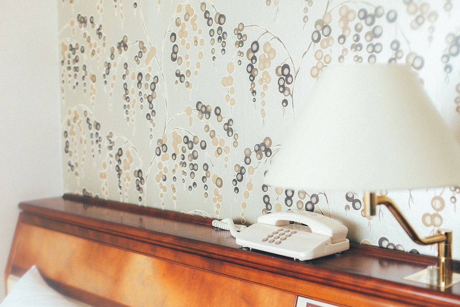 A telephone on a wooden desk with a decorative lamp beside it.