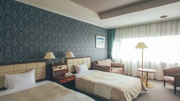A hotel room with two beds, a desk with a telephone, a chair, a small round table, and a lamp.