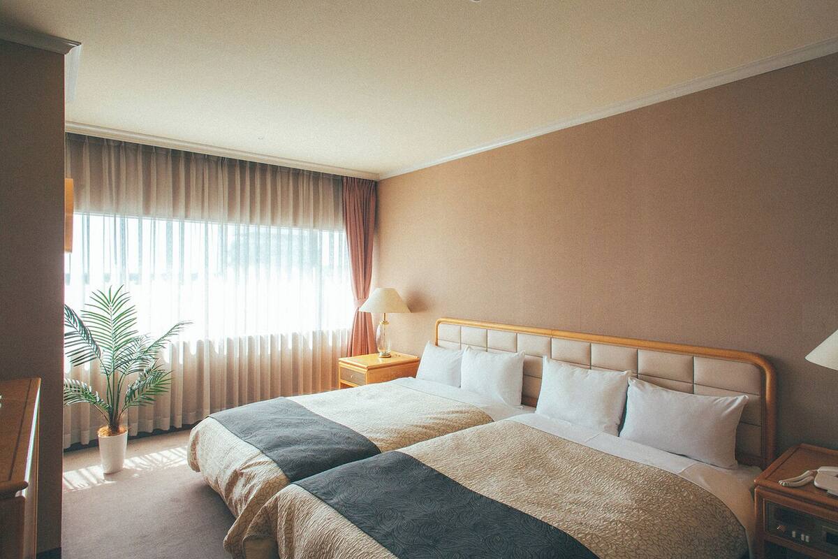 Una camera d'albergo con un letto grande, un comodino, una lampada e una pianta in vaso.