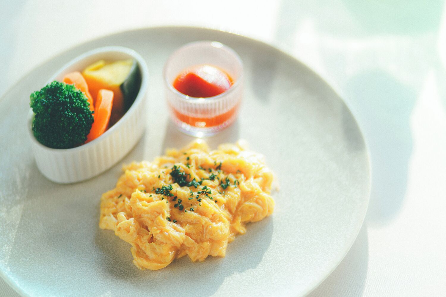 A plate with scrambled eggs, a small bowl of mixed vegetables, and a small container of sauce.