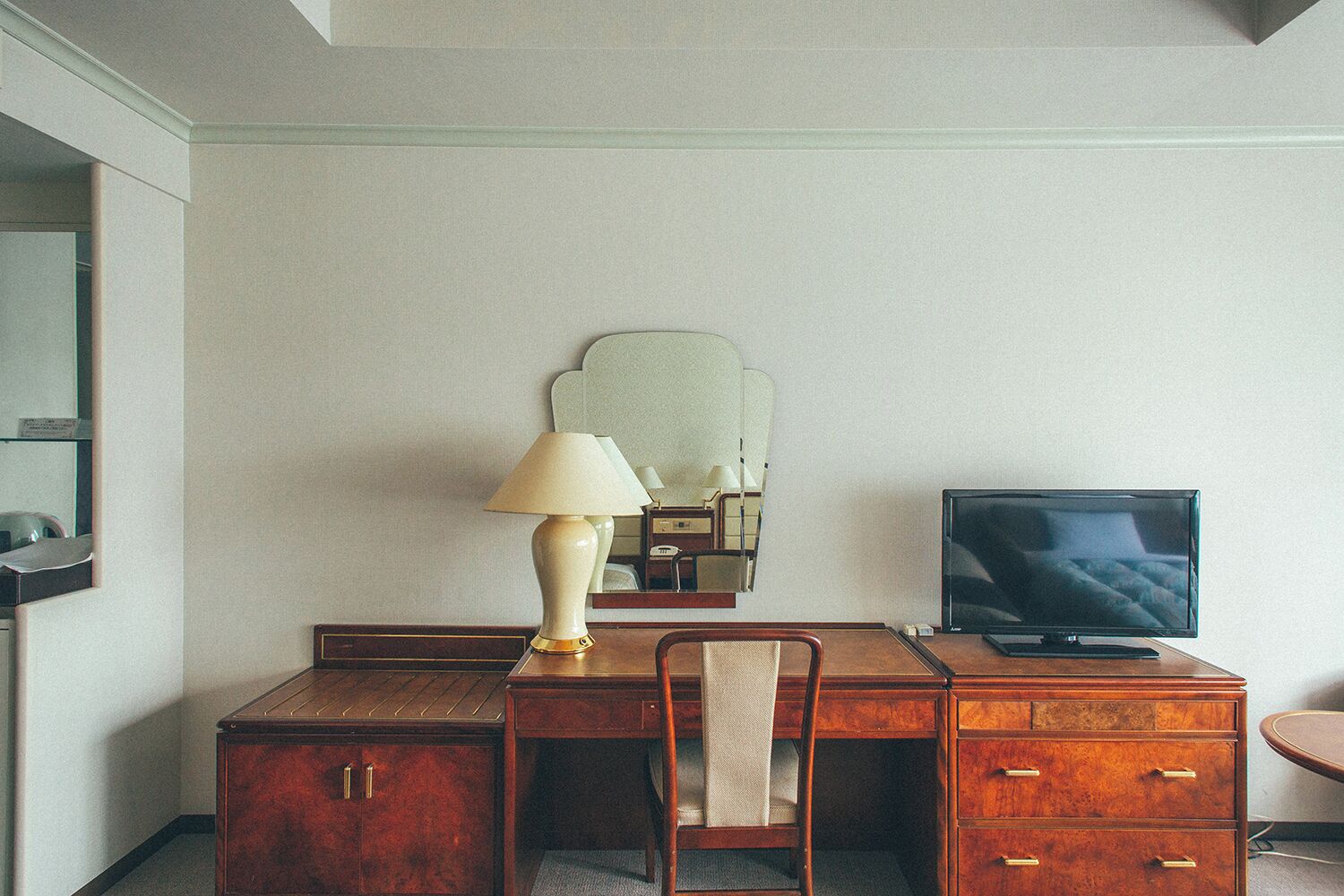 Una habitación de hotel con un escritorio de madera, una silla, una lámpara, un televisor y un espejo.