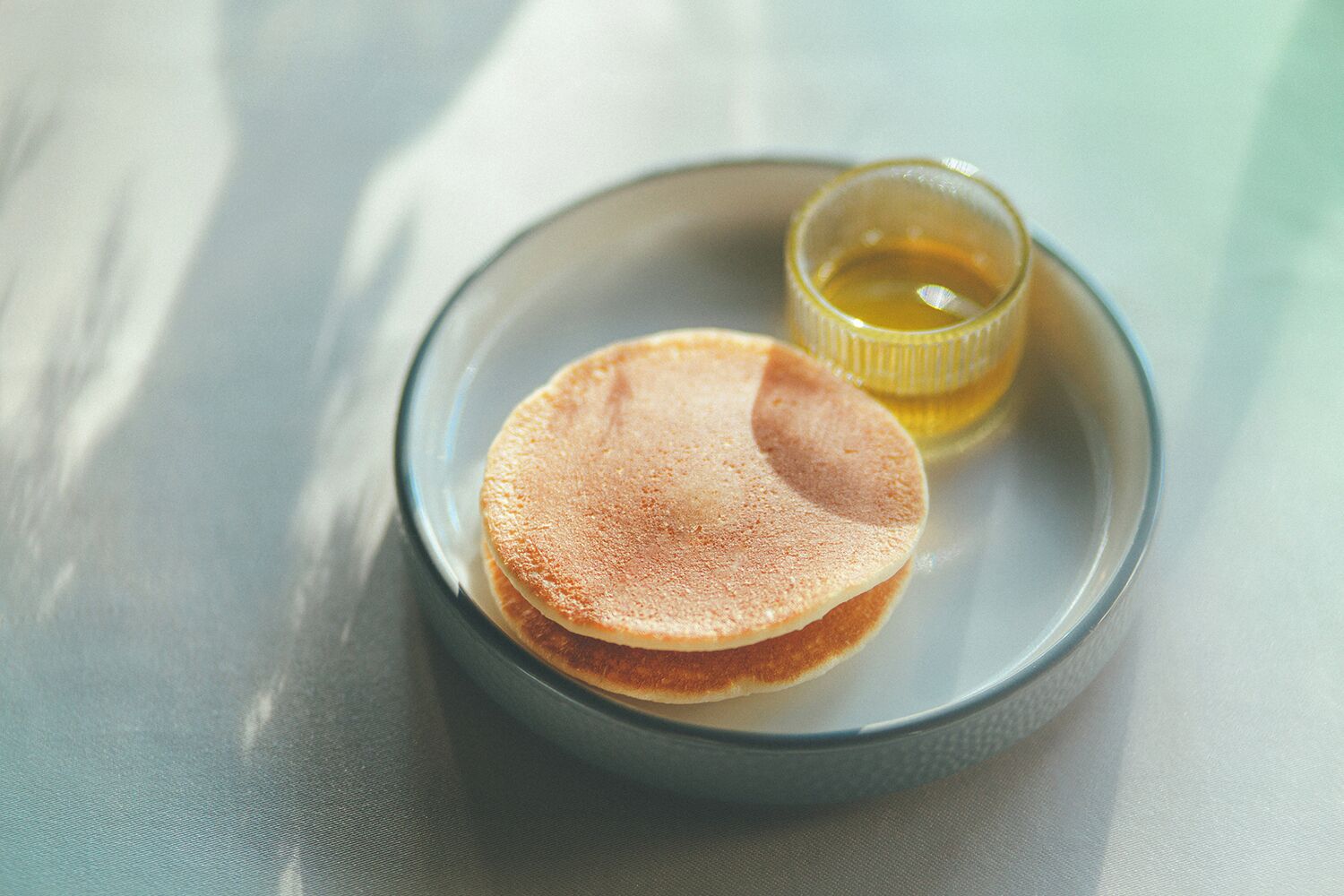 A plate with two pancakes and a small cup of syrup.