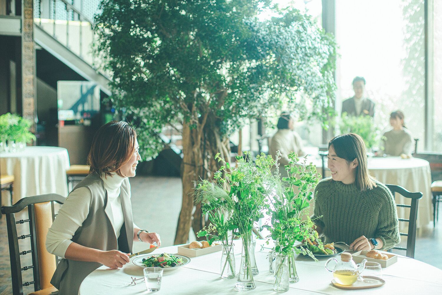Un comedor con mesas, sillas y plantas en macetas.