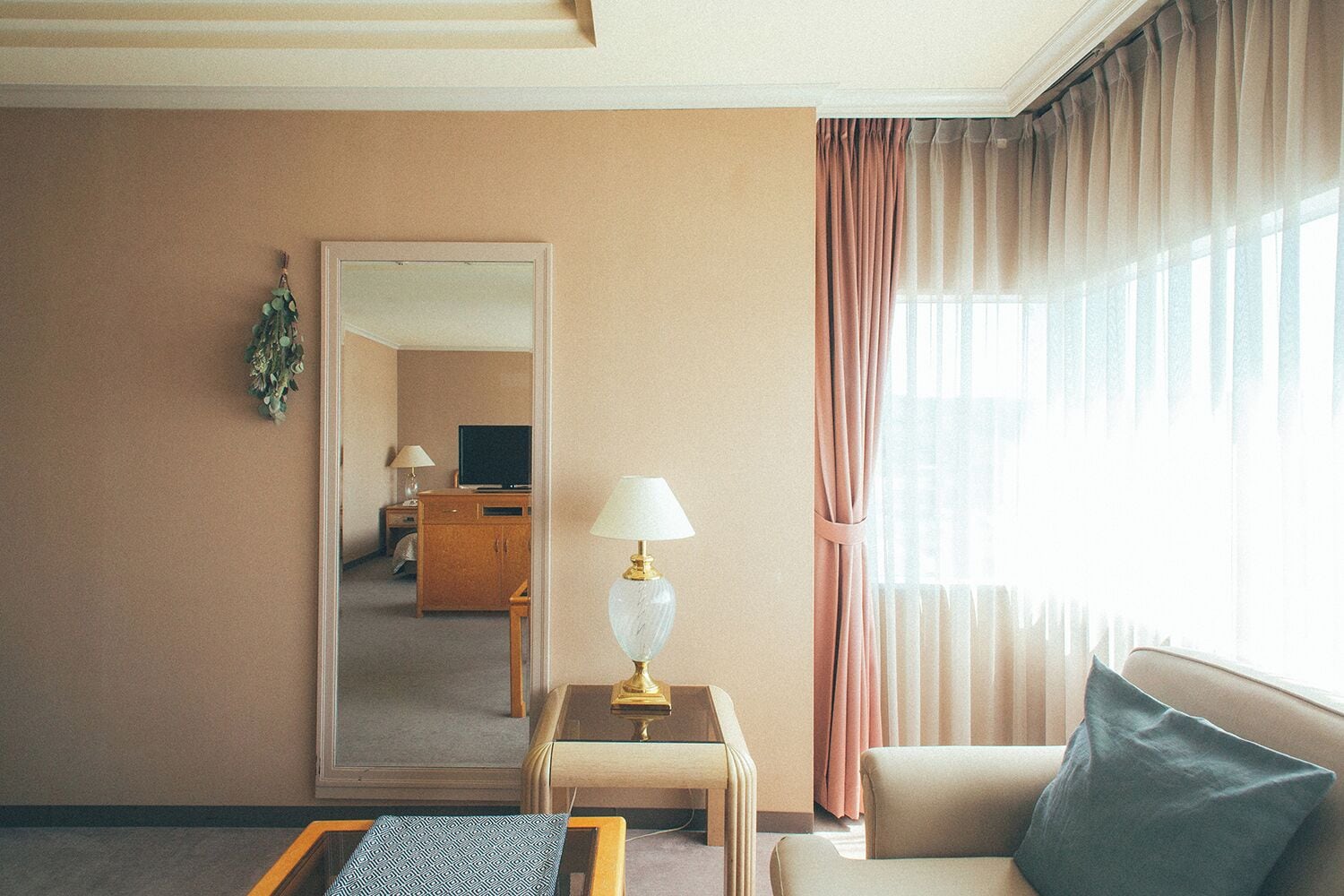 Ett hotellrum med en stor spegel, en soffa, ett bord med en lampa och en tv i bakgrunden.