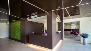 A modern reception area with a green wall, a reception desk, and a seating area with red chairs. - Wellness Hotel Casa Barca - Adults Only (Malcesine)
