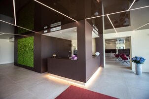 Un área de recepción moderna con una pared verde, una mesa de recepción y un espacio de estar con sillas rojas.