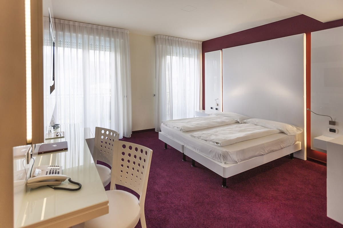 A hotel room with a bed, a desk with a telephone, and a chair.