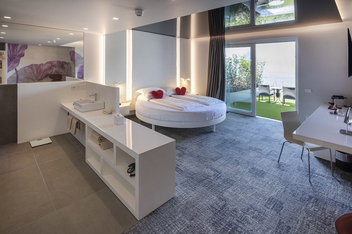 A modern bedroom with a large bed, a white vanity, and a dining area.