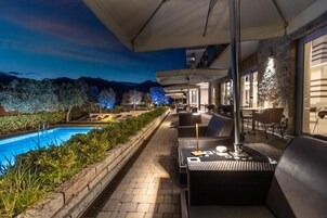 Un patio exterior con piscina, mobiliario y vistas a las montañas.