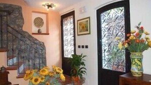 A staircase with a decorative metal railing, a vase with sunflowers, and a door with intricate metalwork. - Mamma Maria (Taormina)