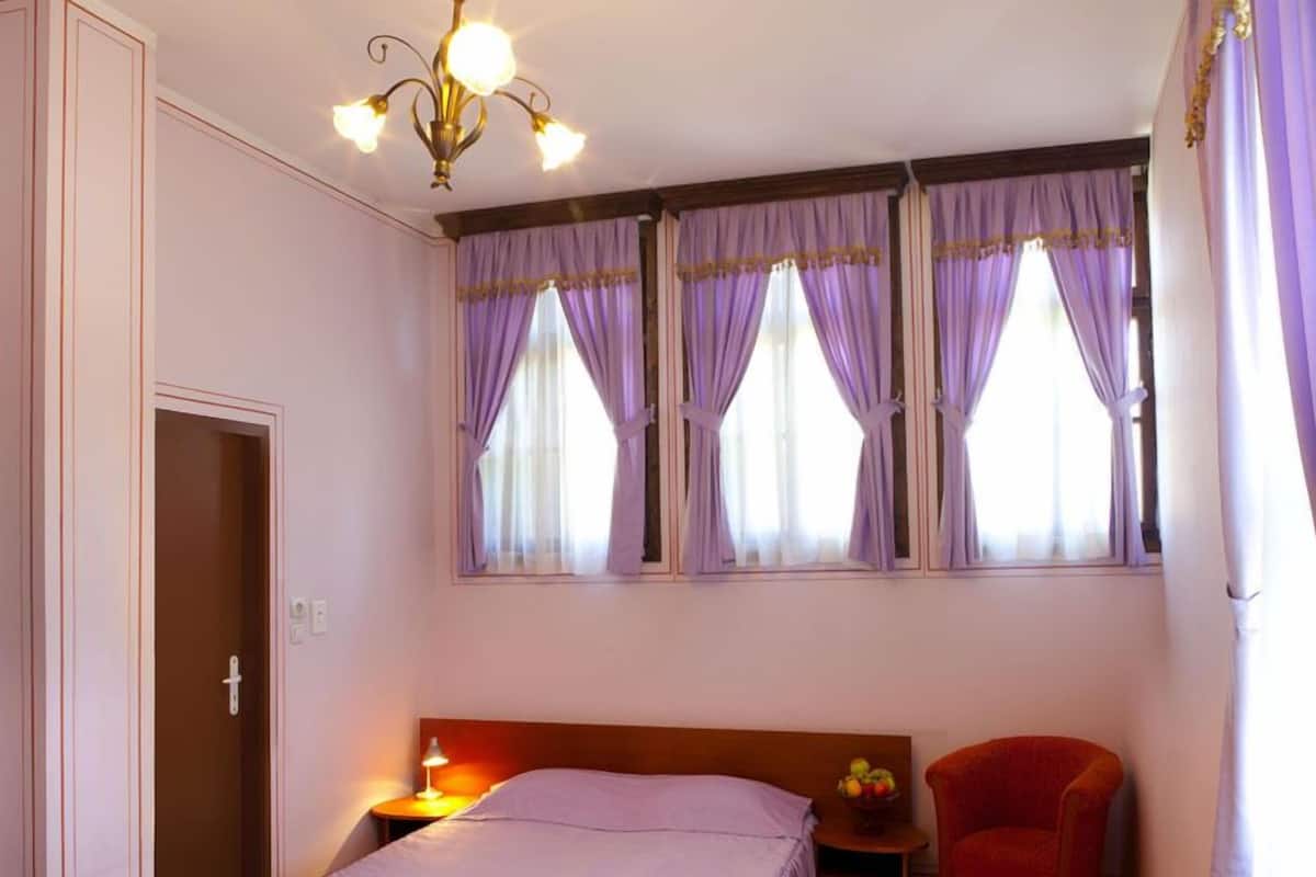 A bedroom with a bed, a nightstand, a chair, and a window with curtains.
