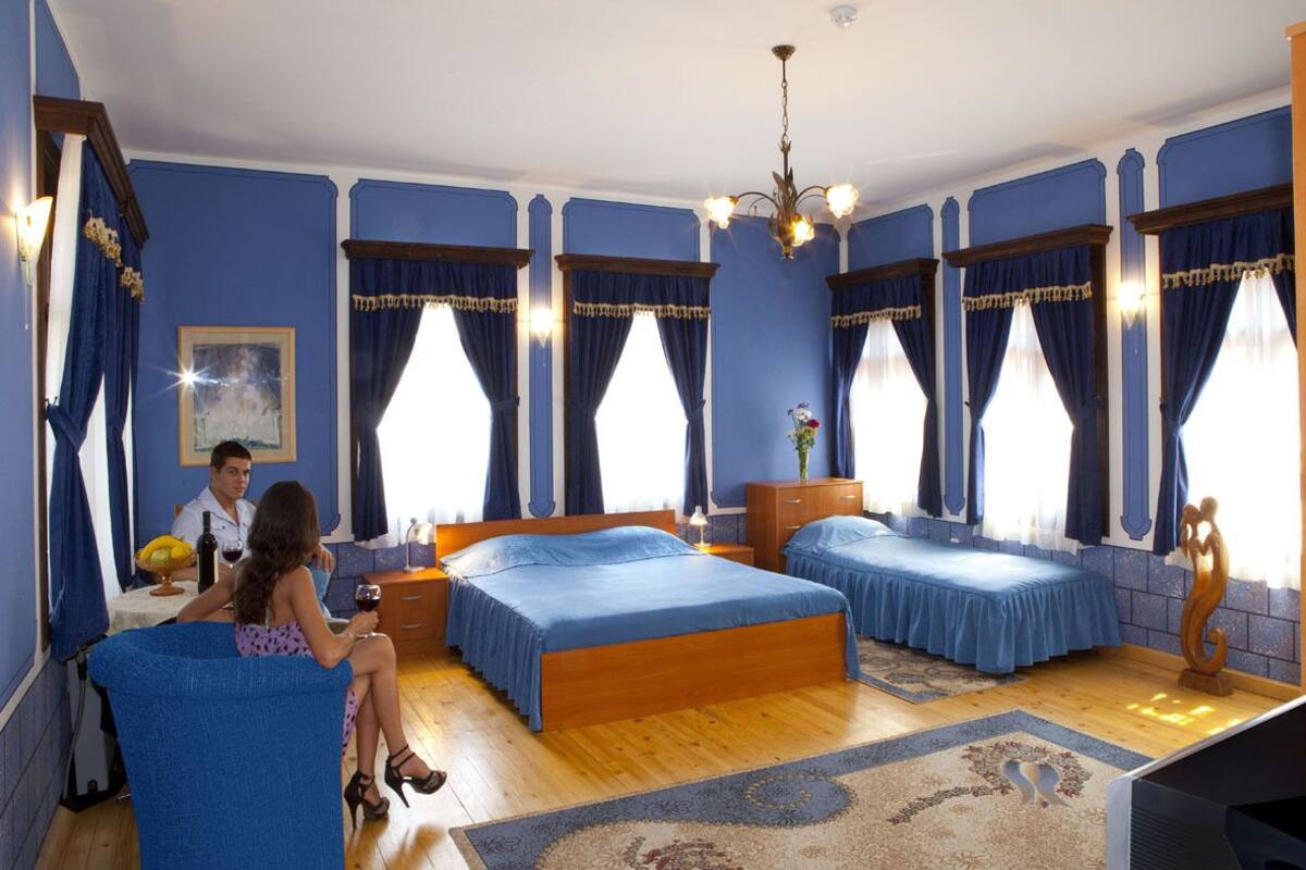 A bedroom with two beds, a chandelier, and a large window with curtains.