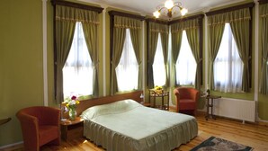 A bedroom with a bed, a chair, a nightstand, a table with a bottle, and a vase with flowers. - Belle Ville (Plovdiv)