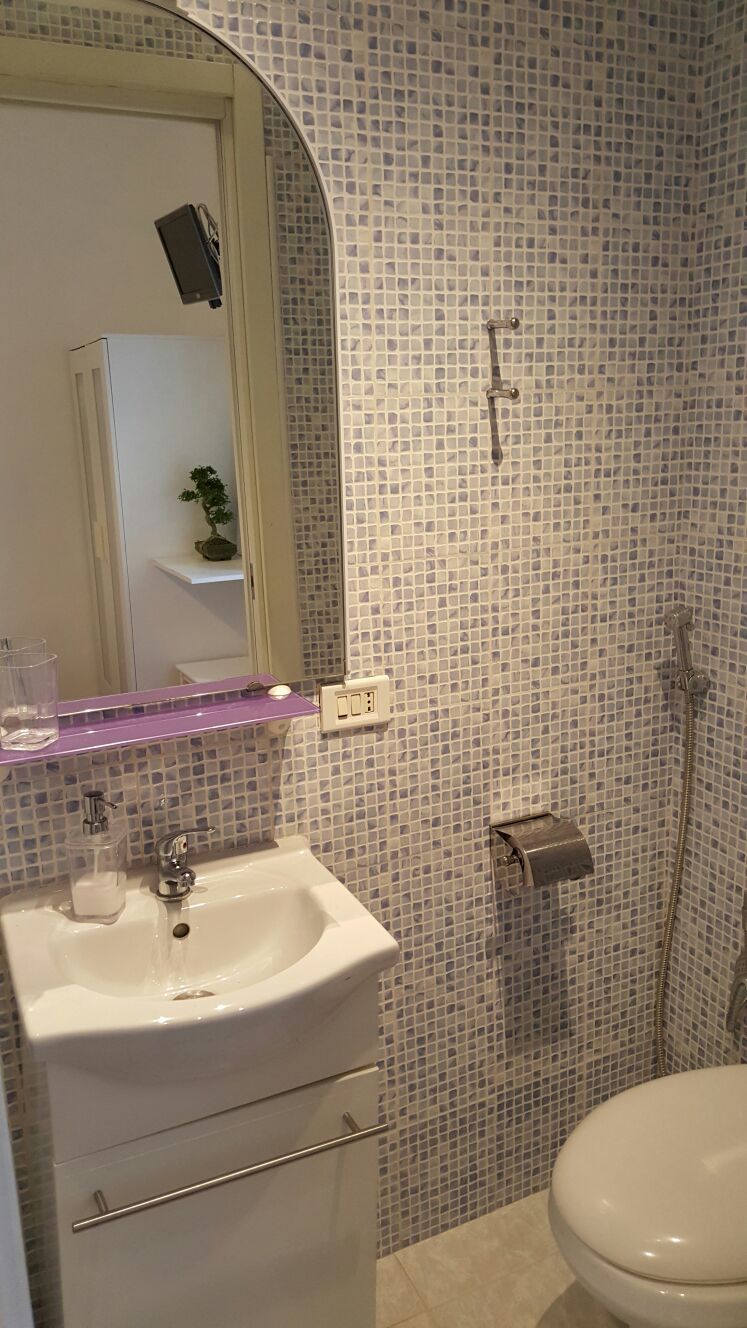 A bathroom with a white sink, mirror, and toilet. The walls are covered with small mosaic tiles.