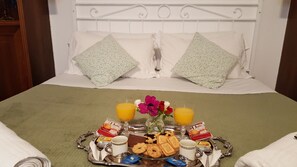 A neatly made bed with a green bedspread, two decorative pillows, a tray with breakfast items including pastries, juice, and a chocolate bar, and a vase with flowers. - Al Ponte del Papa Bed and Breakfast (Rome)