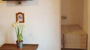 A small room with a wooden table and two white chairs, a TV mounted on the wall, a small potted plant, and a sign with a Wi-Fi password. - Al Ponte del Papa Bed and Breakfast (Rome)