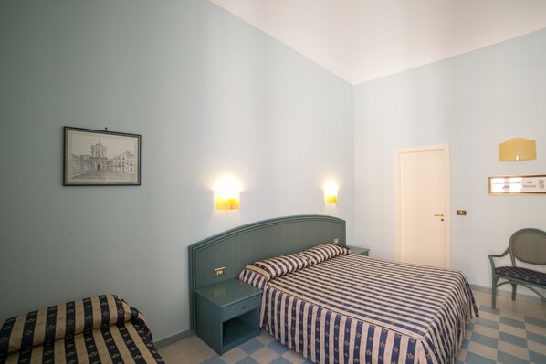 A bedroom with a bed, two bedside tables, a chair, a door, and a framed picture on the wall.