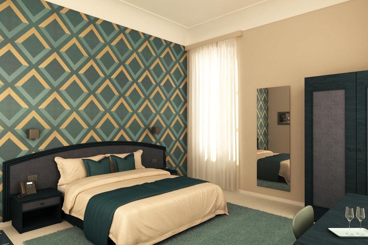 A hotel room with a large bed, a bedside table with a phone, a mirror, and a desk with two wine glasses.