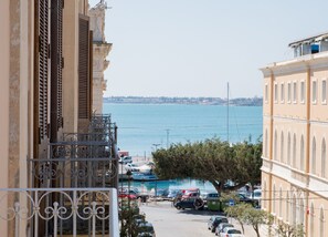 A coastal view with a marina, parked cars, and buildings with balconies overlooking the sea. - Gran Bretagna Boutique Hotel Ortigia (Syracuse)