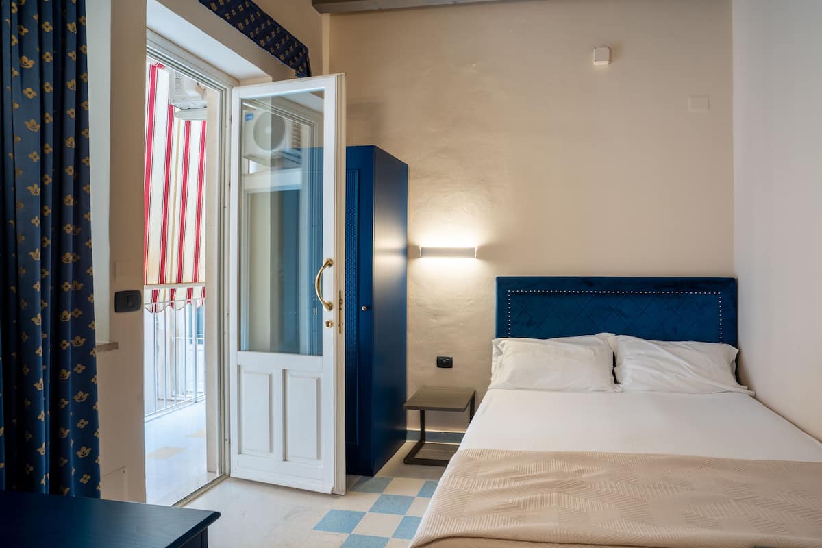 A hotel room with a bed, a wardrobe, a door leading to a balcony, and a small table.