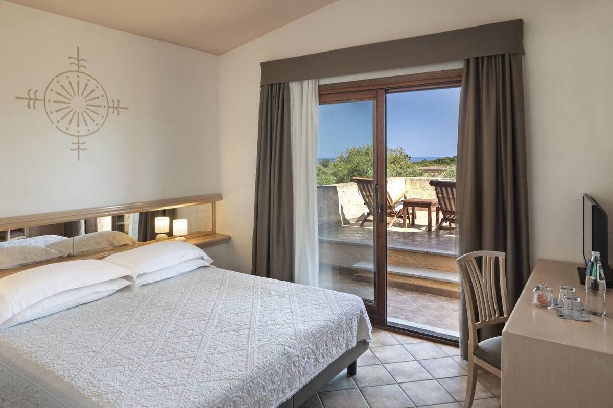 A hotel room with a bed, a desk with a chair, and a view of the outdoors.