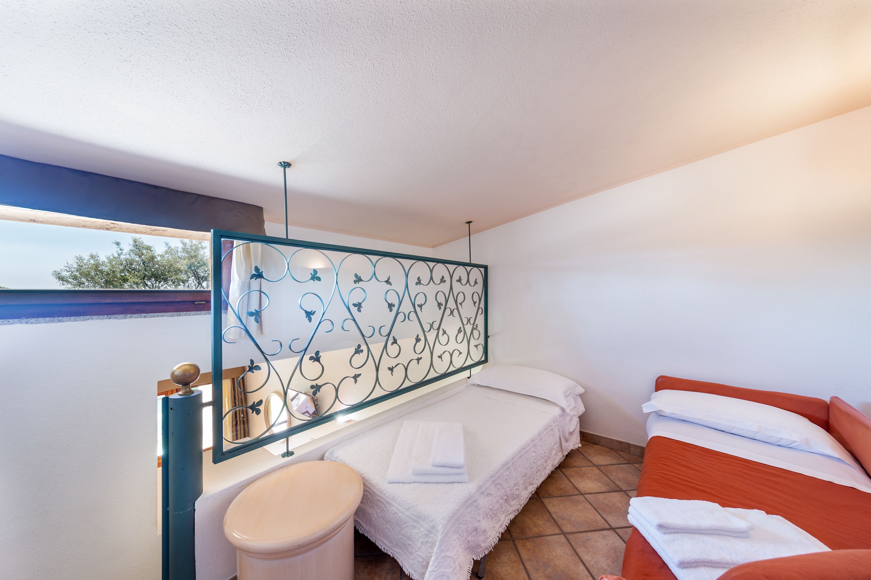 Ein kleines Hotelzimmer mit einem Bett, einem kleinen Tisch, einer Toilette und einem Fenster mit Blick auf Bäume.