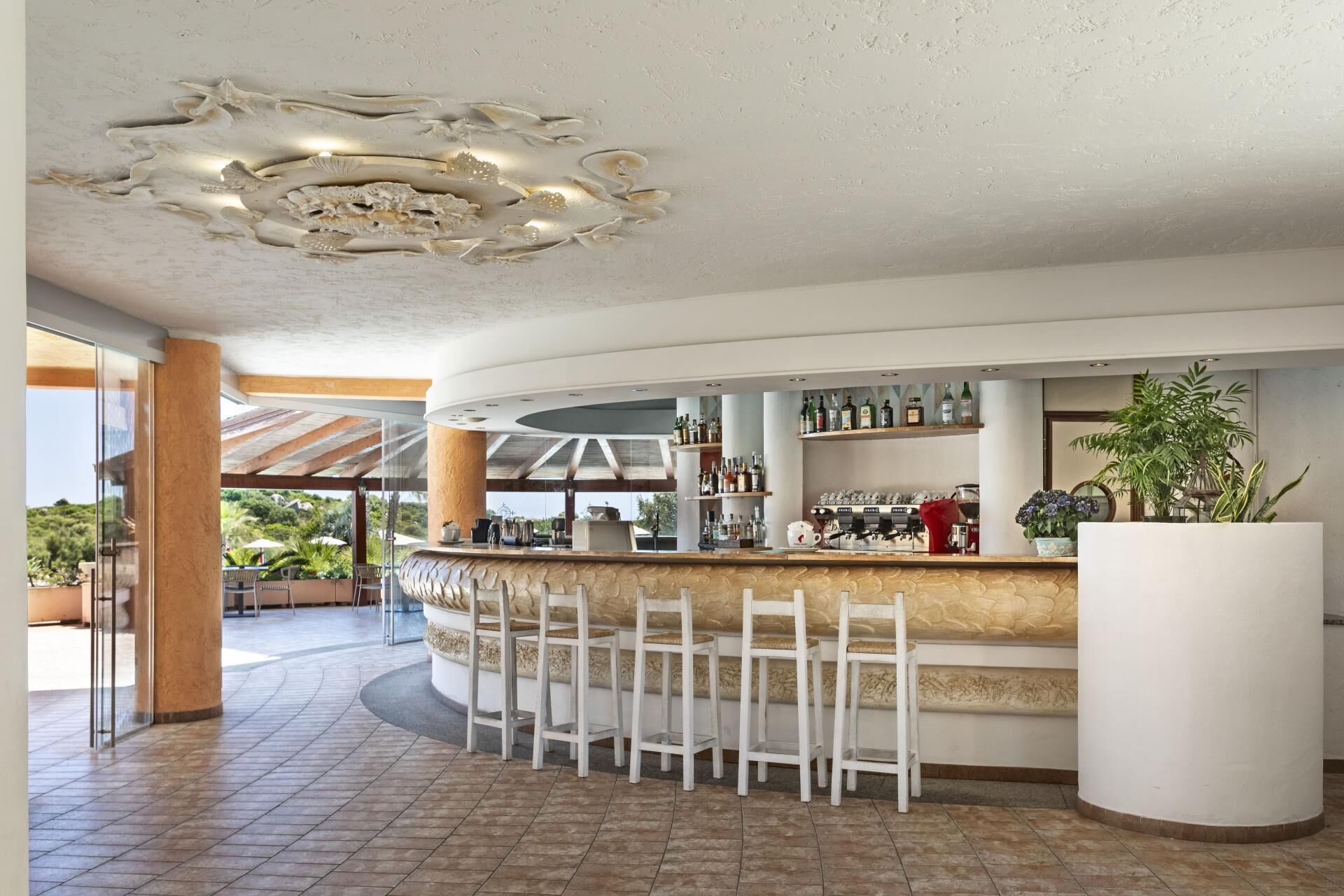 Un espace bar doté d’un comptoir incurvé, de tabourets de bar blancs et d’un plafond orné d’un luminaire original.
