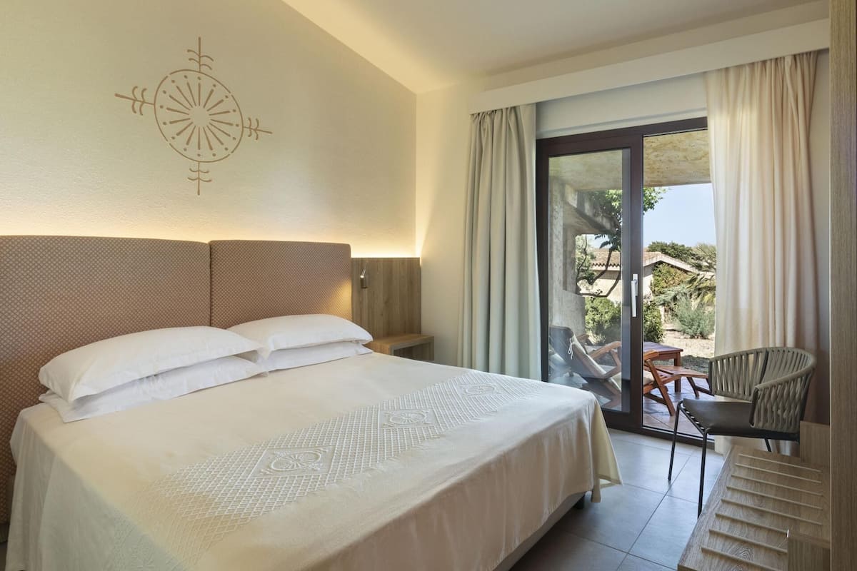 A hotel room with a large bed, a chair, a table, and a view of the outdoors.