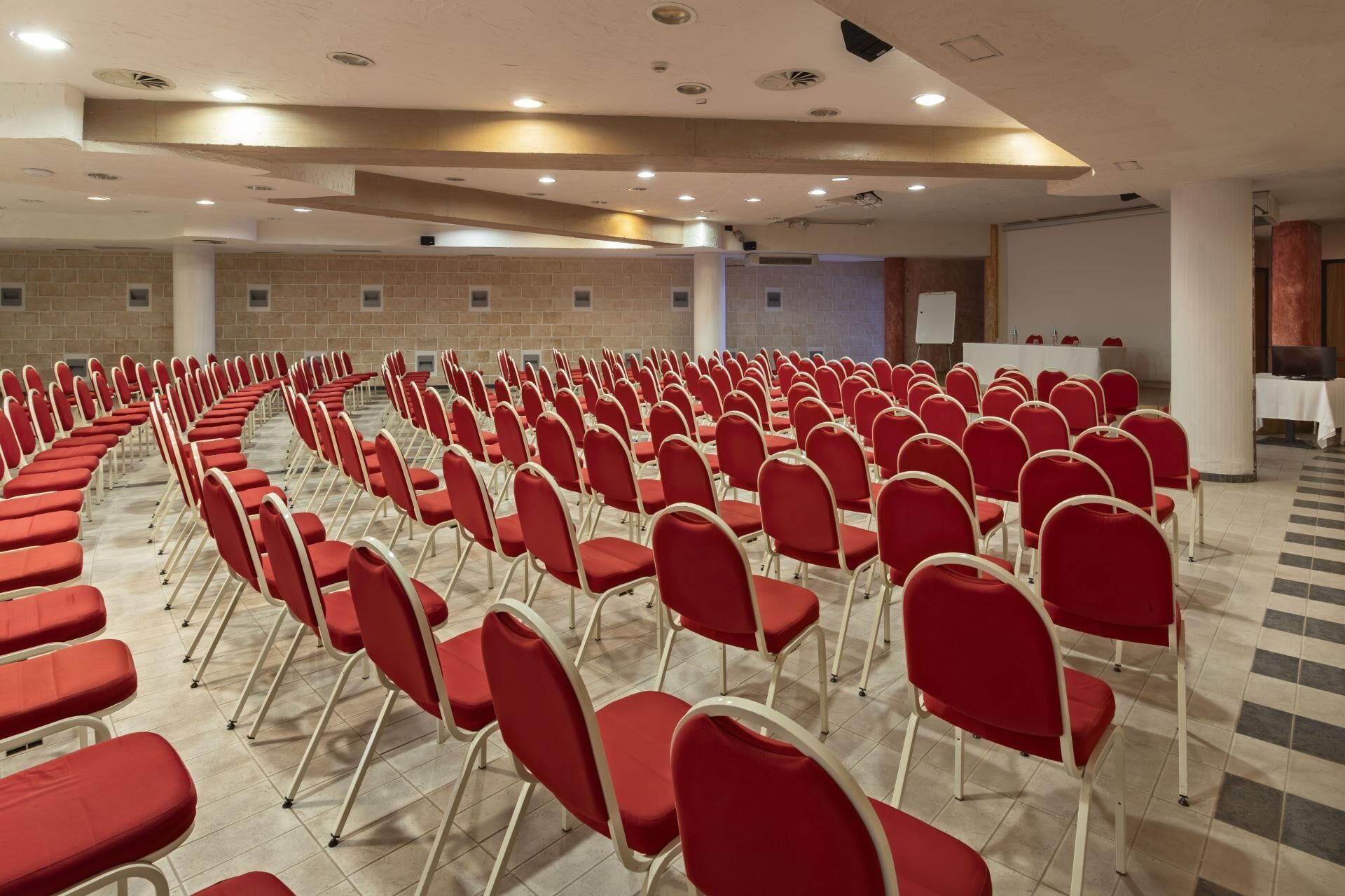 Ein Konferenzraum mit Reihen roter Stühle, einer Tafel und einer Projektionsleinwand.