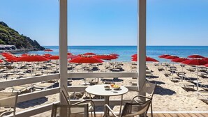 A beachside patio with tables and chairs, red umbrellas, and a view of the sea. - Sant'Elmo Beach Hotel (Castiadas)
