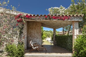 A covered outdoor seating area with stone walls, a pergola, and a view of the surrounding landscape. - Sant'Elmo Beach Hotel (Castiadas)