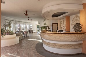 A reception area with a curved reception desk, ceiling fans, and a large wall mural. - Sant'Elmo Beach Hotel (Castiadas)