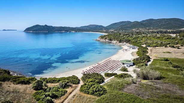 A coastal beach with a clear view of the sea, a sandy shore, and a path leading to a building with multiple rooms. - Sant'Elmo Beach Hotel (Castiadas)