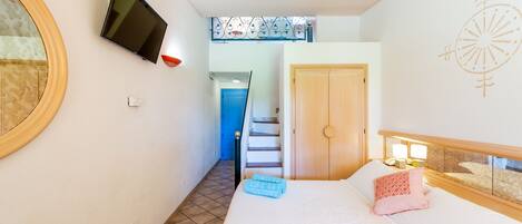 Une chambre à coucher avec un lit, un téléviseur fixé au mur, un escalier menant à une autre pièce et une porte.