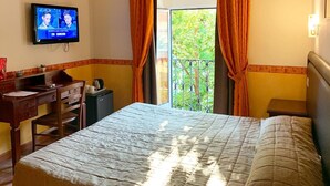 Habitación de hotel con cama, escritorio con silla, televisión y balcón con cortinas.