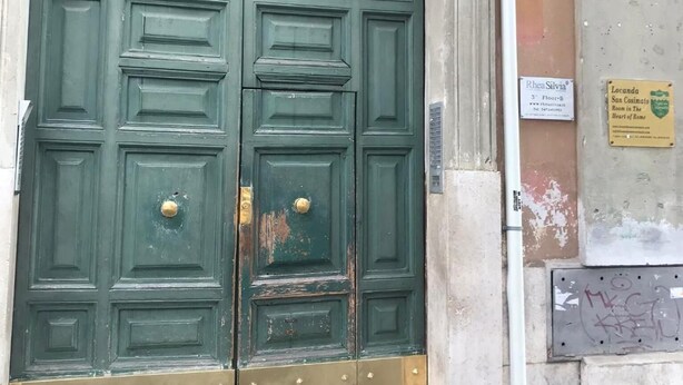 Una puerta doble grande, de color verde, con una celosía metálica decorativa sobre ella, ubicada en un arco de piedra.